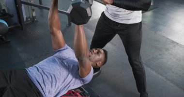 Afrikalı Amerikalı kişisel antrenör, spor salonunda halterlerle ağırlık kaldırarak müşteri kürsüsüne rehberlik ediyor. Spor, güç, antrenman, antrenman, koçluk, sağlık, spor