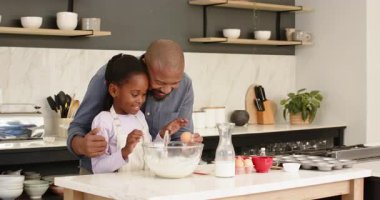 Mutfakta Afrikalı Amerikalı baba, kızına yumurta kırma ve hamuru çırpma konusunda rehberlik ediyor. Aile, bağ, eğitim, yemek pişirme, işçilik, sade, neşeli