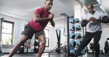 Afrika kökenli Amerikalı antrenör müşterileri dizlerinde yükseltiyor, hamleler yapıyor, grup spor salonunda ısınıyor. Güç, zindelik, egzersiz, eğitim, spor, kas gücü, motivasyon.
