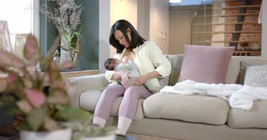 Bej kanepeye bebek bakıcılığı ve battaniye serilmesi için bebeği yerleştiren bir kadın. Annelik, bağlılık, bakım, konfor, ev, şefkat, bakım.