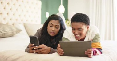 Yatakta yatan çeşitli bayan arkadaşlar, biri tabletten tablete gülümsüyor, diğeri de akıllı telefonları dinliyor. Gündelik, arkadaşlık, iletişim, rahatlama, teknoloji, modern, samimi