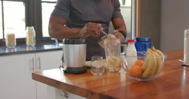 Kıdemli Afro-Amerikalı adam evde meyve püresi yaparken muz dolu blender içine fındık ezmesi sürüyor. Sağlıklı, zindelik, beslenme, yaşam tarzı, sağlık, mutfak, modern