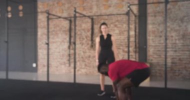 Afrika kökenli Amerikalı antrenör ipleri tutuyor ve kadın müşteriyi halat dalgalarına doğru yönlendiriyor. Spor, güç, koçluk, eğitim, fonksiyonel, atletik, motivasyon