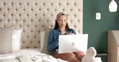 Anne akıllı telefondan sesli mesaj kaydediyor, dizüstü bilgisayarı kontrol ediyor ve bebeği yatakta izliyor, boşluğu kopyalıyor. Ebeveynlik, çoklu görev, samimiyet, rahatlama, konforlu, dijital, çocuk odası