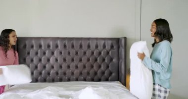 Yatak odasında beyaz yorgan ve deri yatak başlığıyla yatak hazırlayan bayan arkadaşlar. Samimiyet, dostluk, iç mekan, rahatlama, rahat, sıcak, sosyal