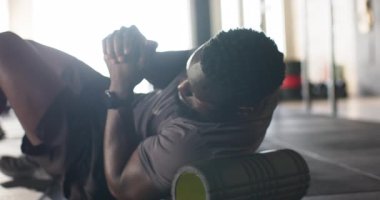 Afrikalı Amerikalı bir adam spor salonunda gövdenin altına köpük paten yerleştirip kas gerilimi yaratıyor. Zindelik, iyileşme, kendine bakım, esneklik, güç, sağlık, eğitim