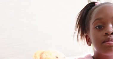 Afrikalı Amerikalı bir kız oyuncak ayıya sarılıyor ve yatak odasında sırıtıyor. Çocukluk, masumiyet, arkadaşlık, duygusal, ifade, rahatlık, sıcaklık.