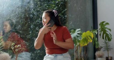 Akıllı telefon çalması Asyalı kadının telefona cevap vermesine ve cam duvardan bahçeye doğru hareketlenmesine neden oluyor. Bitki dekoru, sükunet, refah, dinginlik, doğal ışık, yaşam tarzı, modern iç mekan.