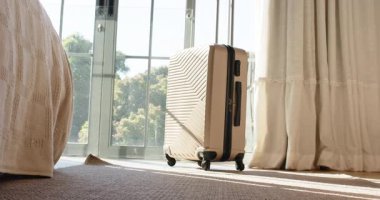 Sabah ışığı cam kapılardan süzülüyor bavul sapını genişletiyor ve kilitlenmeye hazır hale getiriyor. Bagaj, seyahat, seyahat takımı, modern, minimalist, açık hava, güneş ışığı