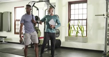Spor salonuna girerken, Afrikalı Amerikalı antrenör müşteriyi tablet üzerinde çömelmiş raf planlama egzersizine yönlendiriyor. Fitness, antrenman, akıl hocalığı, güç, motivasyon, sağlık, spor