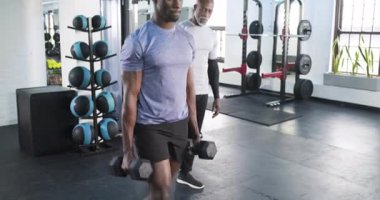 Afrika kökenli Amerikalı erkek antrenör, müşterinin jimnastik salonunda yumruk tokuşturma hareketini işaret ediyor. Güç, dayanıklılık, motivasyon, işbirliği, atletizm, refah, fitness