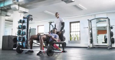 Afrika kökenli Amerikalı müşteri antrenör rehberliğinde halterle ağırlık kaldırmaya yaklaşıyor. Zindelik, güç, kişisel eğitim, spor, egzersiz, kas gücü, kararlılık