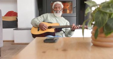 Yaşlı Afro-Amerikan adam gitar tıngırdatıyor, şarkı söylüyor ve rahatlamak için odun sobası başında gülümsüyor. Konforlu, ahenkli, akustik, boş, kırsal, sağlıklı, melodi