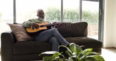 Olgun bir Afrikalı Amerikalı akustik gitarla akorları değiştirip pratik yapıyor. Melodi, rahatlama, kırsal, akustik, boş zaman, yaşam tarzı, dekor