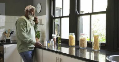 Yetişkin bir Afro-Amerikalı telefon görüşmesi yapıyor. Mutfak tezgahında su ile ilaç alıyor. Sağlık, sağlık, modern, yaşam tarzı, rutin, iç, beslenme