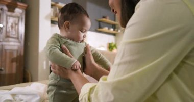 Anne küçük kızını bej kanepede kucağına alıp oturma odasında baldırların üzerinde alıştırma yapıyor. Sarılma, gelişme, bağlanma, beslenme, sıcaklık, şefkat, çocukluk