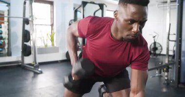 Kürsüye yaklaşan Afro-Amerikan adam, sırt ağrısı için spor salonunda dambıl sırtı hareketi yapıyor. Spor, güç, antrenman, spor, spor, spor, sağlık.