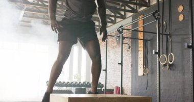 Çömelmiş, Afrikalı Amerikalı bir adam spor salonundaki güç arttırıcı kutunun üstüne atlıyor. Fitness, antrenman, atletik, patlayıcı, güç, dinamik, spor