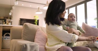 Asyalı anne ve kız bebek kanepede oturmuş oyun için pelüş top oyuncaklarını sallıyorlar. Ebeveyn-çocuk, bağlanma, beslenme, samimiyet, evcil, samimi, hassas