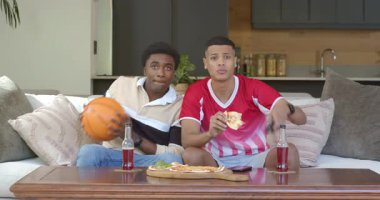 Kanepede kola yudumlayan çeşitli erkek arkadaşlar TV sürpriziyle basketbol kumandasını kapıyor. Sıradan, yoldaşlık, eğlence, eğlence, yaşam tarzı, iç mekan, mutluluk.