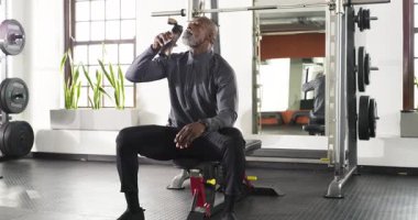 Afrika kökenli Amerikalı son sınıf öğrencisi jimnastik salonunda dinleniyor, sallanan şişeden içiyor ve gülümsüyor. Spor, sağlık, güç, motivasyon, aktif, yaşam tarzı, sağlık