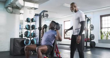 Afrikalı Amerikalı antrenör, müşteriye beden eğitimi dersinde başınızın üstündeki dambıllara güç vermesi için baskı yapıyor. Güç, fitness, egzersiz, eğitim, zindelik, egzersiz, koç