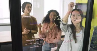 Çeşitli iş arkadaşları toplandıktan sonra cam levhada işaretleyici kullanarak plan yapmak için beyin fırtınası yapıyorlar. İşbirliği, yenilik, takım çalışması, beyin fırtınası, modernlik, iletişim, stratejik