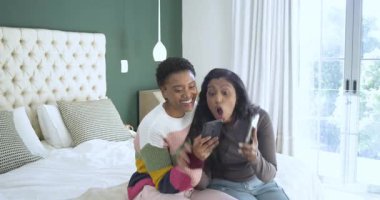 Güneşli yatak odası. İki kadın şakalaşmak için telefona uzanıyor. Yatağa düşüyorlar ve gülüyorlar. Arkadaşlık, arkadaşlık, rahatlama, modern, samimi, samimi, canlı.