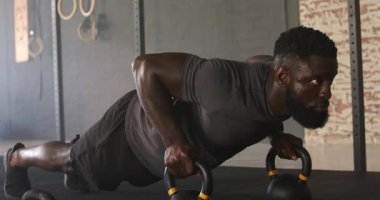 Afrika kökenli Amerikalı bir adam lastik zemine kettlebell yerleştiriyor sonra da çekirdek gücü için şınav çekiyor. Güç, fitness, egzersiz, antrenman, spor, egzersiz, atletizm