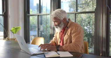 Dizüstü bilgisayarın açılışında kıdemli Afro-Amerikalı adam pencerenin yanındaki masada geri bildirim bekliyor. Profesyonel, işyeri, modern, boş zaman, güneşli, yansıtıcı, dijital