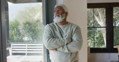 Güverte manzaralı Afro-Amerikan adam dönüyor, ağaçlara bakan cam kapıyı yansıtıyor. Düşünce, sükunet, doğa, sükunet, farkındalık, ev, kırsal