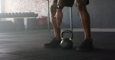 Afrikalı Amerikalı bir adam çömelmiş, kettlebell 'i tutuyor, spor salonunda güç için temizlik yapıyor ve üstten bastırıyor. Güç, zindelik, antrenman, spor, atletizm, azim, kas