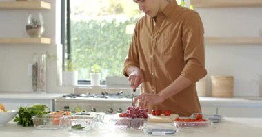 Yetişkin adam kırmızı üzümlere uzanıyor ve mutfak adasında aperatif hazırlarken tahtayı kesiyor. Aşçılık, aşçılık, yemek hazırlama, sağlıklı beslenme, yaşam tarzı, minimalist, enerjik