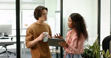 Çalışma odasındaki cam duvarın yanında inceleme, el kol hareketi ve kaydırma için tablete bakan çeşitli iş arkadaşları. İşbirliği, iletişim, takım çalışması, modern, profesyonel, yenilik, tartışma