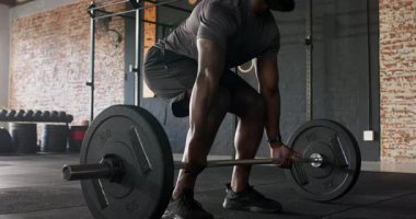 20 'li yaşlarda spor salonunda dolu halteri fark edip kaldırma hareketi yapan Afrikalı Amerikalı bir adam. Güç, zindelik, performans, eğitim, erkeksi, kaslı, güçlü kaldırma