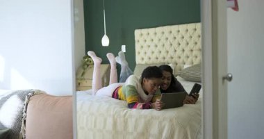 Parlak yatak odasında yatan çeşitli kadın arkadaşlar tablet üzerindeki komik içerikleri inceliyorlar. Gündelik, dostluk, rahatlama, rahat, doğal ışık, ev, yaşam tarzı