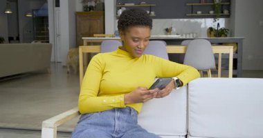 Afro-Amerikalı kadın kanepeye kıvrılıp eğlenmek için kahverengi köpekle gülümsüyor. Gelişigüzel, rahatlatıcı, modern, yaşam tarzı, yerli, samimi, teknoloji