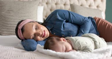 Çeşitli anne ve bebek yatak odasındaki şişkin yatakta yatıyorlar, bebek kafası kayıyor ve anne gülümsüyor. Sarılma, samimiyet, dinginlik, şefkat, rahatlık, bakım, huzur