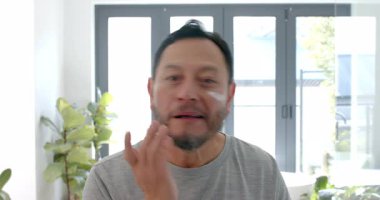 Asyalı olgun bir adam mutfak lavabosunda krem sürüyor ve sabah tenine masaj yapıyor. Cilt bakımı, bakım, sağlık, doğal ışık, minimalist, yaşam tarzı, kişisel bakım