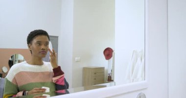 Gösteriş için elinde krema kavanozu tutan Afro-Amerikalı kadın rutin kapak açma ve ovma kremi kullanıyor. Cilt bakımı, güzellik, bencillik, zarafet, minimalizm, cilt bakımı, sağlık