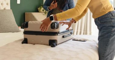 Kadın valiz kapağını indiriyor ve valizi açmak için açtıktan sonra içindekileri yatağa bastırıyor. Seyahat, valiz, organizasyon, ev, yaşam tarzı, modern