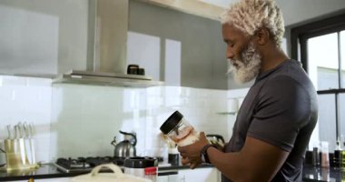 Afro-Amerikalı adam mutfak adasında meyve püresi yapmak için blender tuşuna basıyor. Sağlıklı, yaşam tarzı, canlı, aşçı, modern, sağlıklı, yerli