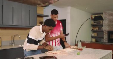 Çeşitli erkek arkadaşlar akıllı telefon kaldırıyor, mermer adada pizza yapıp peynir rendeliyor. Yemek pişirme, takım çalışması, aşçılık, modern mutfak, yaşam tarzı, kutlama, yemek hazırlama