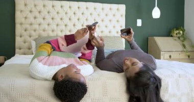 Çeşitli bayan arkadaşlar yatağın üzerinde akıllı telefonları dinliyorlar, diz kaldırma hareketlerini yansıtıyorlar ve kahkahaları paylaşıyorlar. Gündelik, arkadaşlık, rahatlama, modern, rahat, yaşam tarzı, iletişim