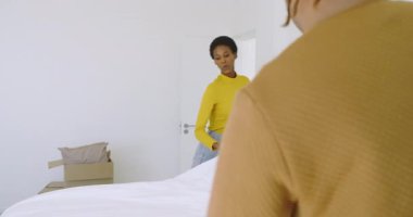 Afro-Amerikan çift yatak odasına kutuyla giriyor ve yatak düzenlemek için yastık ve yatak düzenliyorlar. Ev dekorasyonu, iç tasarım, minimalizm, konforlu, işbirliği, organizasyon, yaşam tarzı