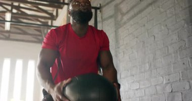 Kırmızı dişli Afro-Amerikan bir adam spor salonuna giriyor top kaldırıyor, güç için duvara fırlatıyor. Spor, güç, dayanıklılık, egzersiz, antrenman, atletizm, egzersiz