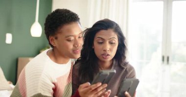 Afro-Amerikan ve Hintli kadınlar akıllı telefonları yatakta karşılaştırıyor, gülüyor ve telefon atıyorlar. Arkadaşlık, kahkaha, bağlantı, eğlence, rahatlama, mutluluk, coşku