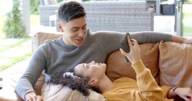 Kahve fincanından içen ve deri koltuktaki akıllı telefondan kayan farklı çiftler kahkahalarını paylaşıyor. Samimiyet, samimiyet, rahatlama, yaşam tarzı, modern, gündelik, bağlantı