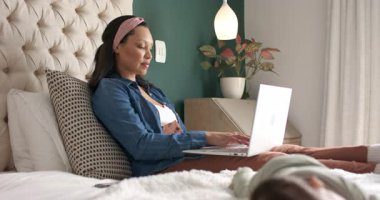 Laptop ekranına bakarken, anne yatakta uyuyan bebeğin yanında iş e-postaları yazıyor. Çalışma akışı, çoklu görev, konfor, ev ofisi, ebeveynlik, dijital, dinginlik
