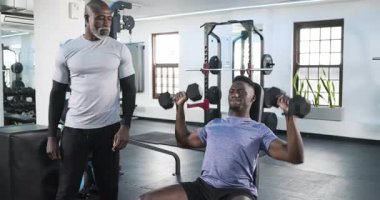 Form düzeltmesi için halterleri kaldıran Afrikalı Amerikalı antrenör müşteriye rehberlik ediyor. Spor, güç, egzersiz, sağlık, koçluk, spor